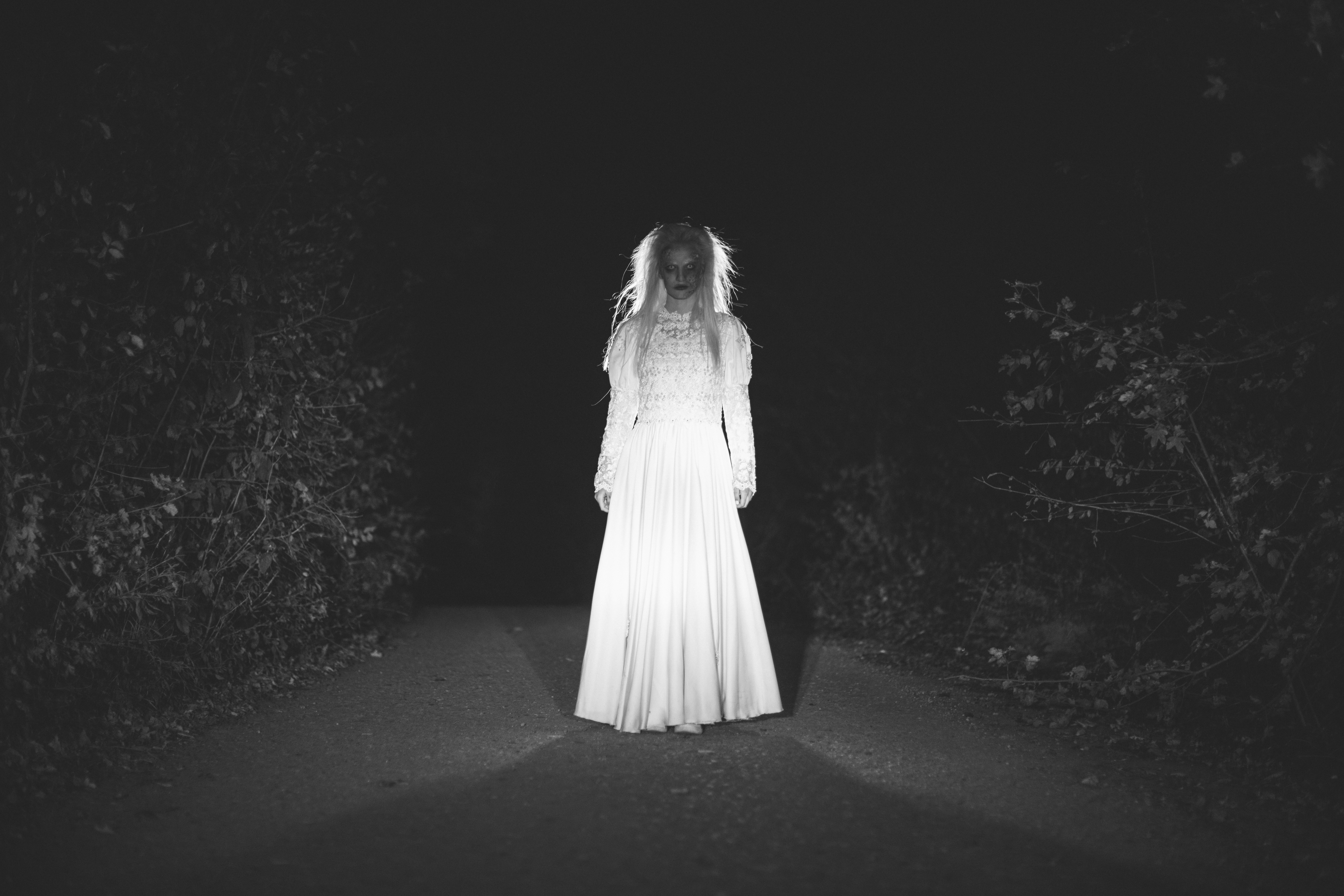 Eine geisterhafte Gestalt im weißen Kleid steht nachts auf einer Straße – inszeniertes Symbolbild.