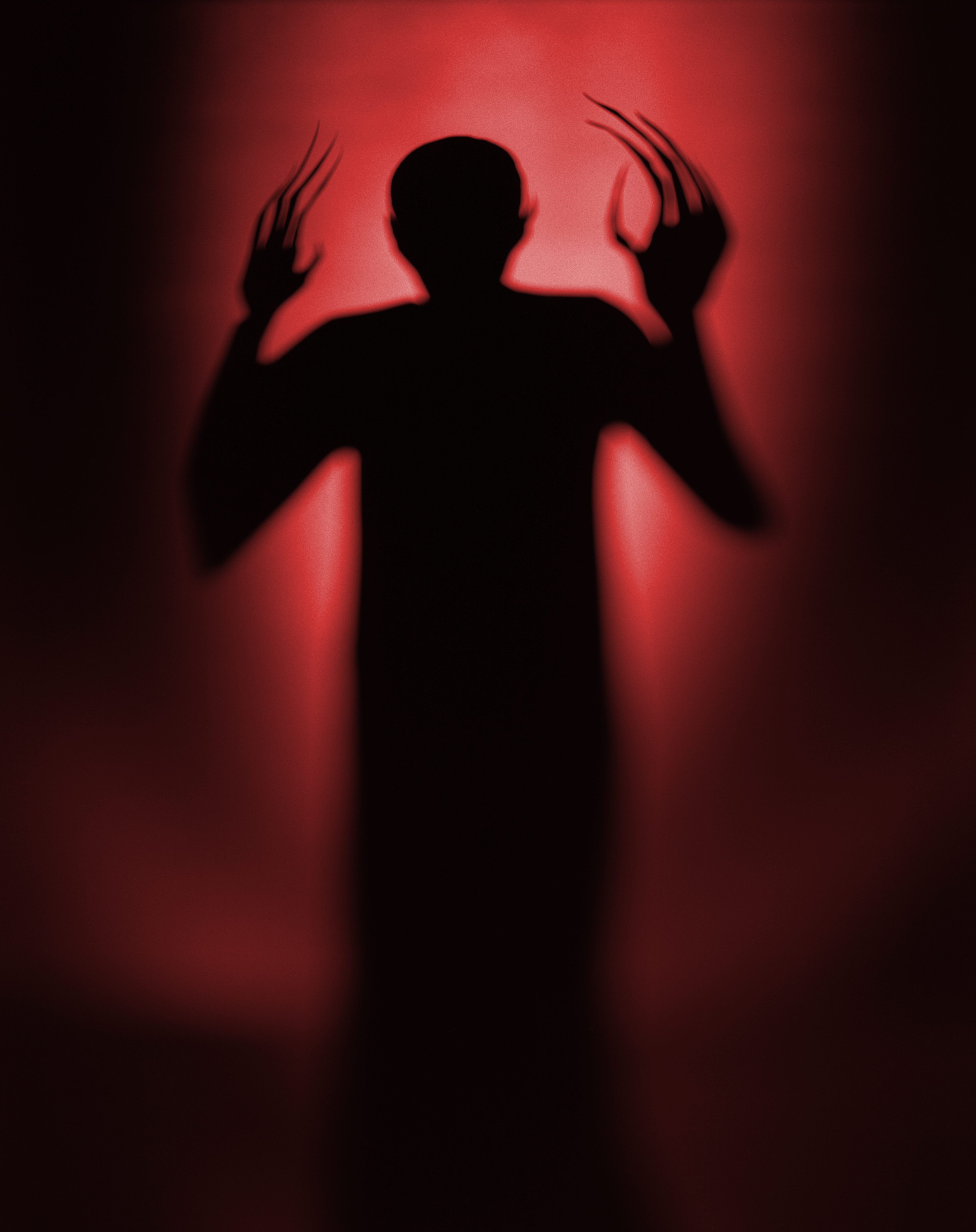 Schatten eines Menschen mit erhobenen Händen vor einer rot beleuchteten Wand.