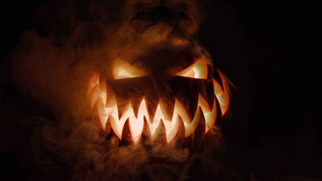 Ein geschnitzter Halloween-Kürbis mit leuchtenden Augen und gezacktem Mund im Rauch.