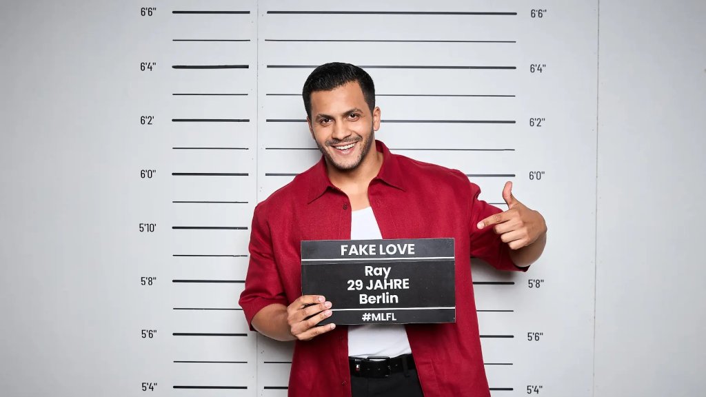 Ray lächelt im roten Hemd beim offiziellen Fotoshooting für „Make Love, Fake Love“.
