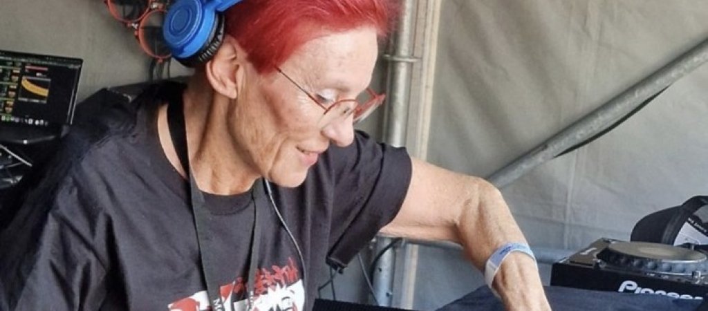 DJ Elly mit roten Haaren und blauen Kopfhörern am Mischpult.