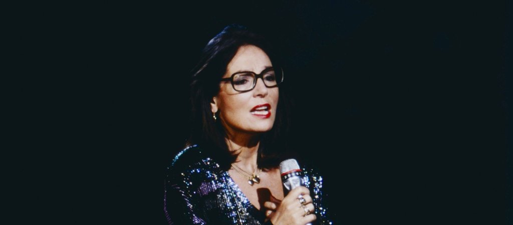 Nana Mouskouri singt mit Mikrofon, markanter Brille und glitzerndem dunklem Kleid auf einer Bühne. Archivaufnahme.