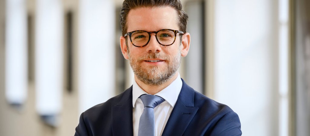 Felix Heinrichs im Anzug vor einem hellen Säulengang