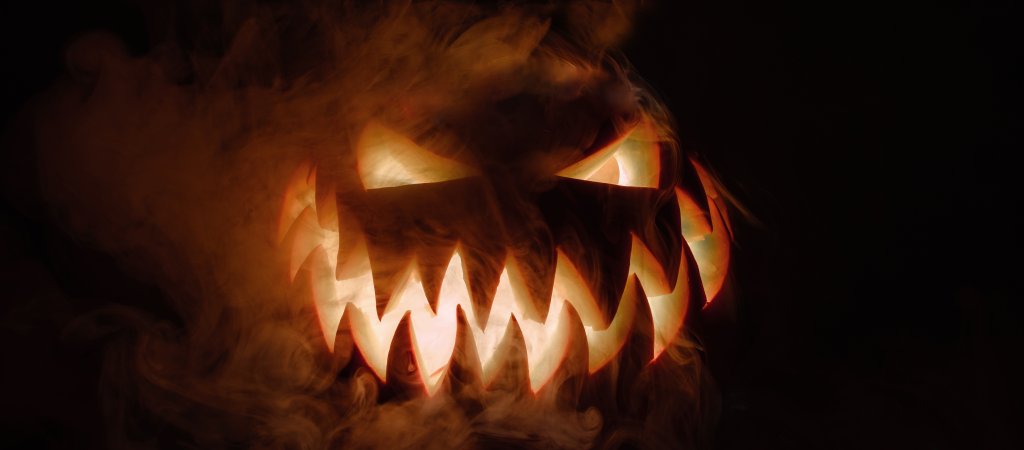 Ein geschnitzter Halloween-Kürbis mit leuchtenden Augen und gezacktem Mund im Rauch.