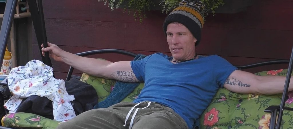 Christian Lell sitzt mit Mütze und blauem T-Shirt im Garten von Promi Big Brother.