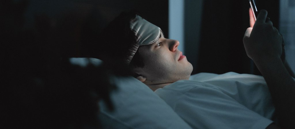 Symbolbild: Ein Mann liegt nachts im Bett und schaut auf sein Smartphone.