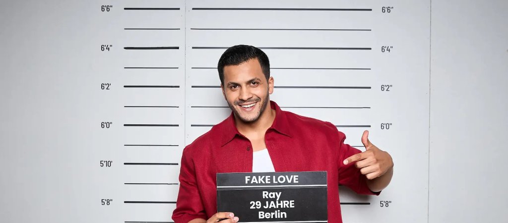 Ray lächelt im roten Hemd beim offiziellen Fotoshooting für „Make Love, Fake Love“.