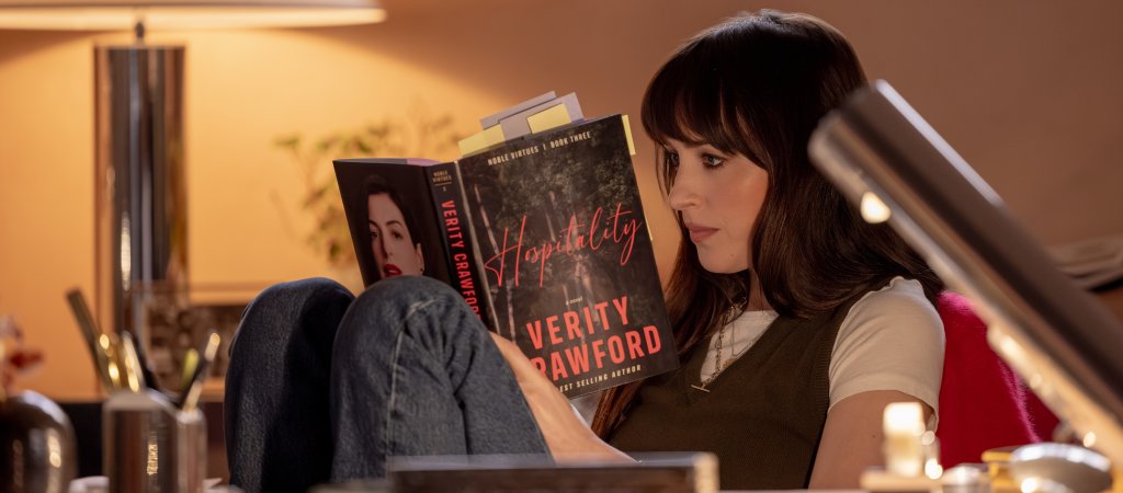 Szenenbild aus „Verity“: Lowen Ashleigh sitzt mit angezogenen Beinen in einem Sessel und liest konzentriert in einem mit zahlreichen Notizzetteln versehenen Buch.