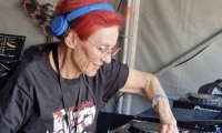 DJ Elly mit roten Haaren und blauen Kopfhörern am Mischpult.