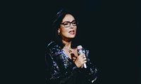 Nana Mouskouri singt mit Mikrofon, markanter Brille und glitzerndem dunklem Kleid auf einer Bühne. Archivaufnahme.