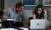 Szenenbild aus „The Social Reckoning“: Ein Mann mit Notizblock und eine Frau sitzen auf einem Sofa und betrachten gemeinsam einen geöffneten Laptop.