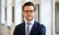 Felix Heinrichs im Anzug vor einem hellen Säulengang