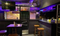 Barbereich des CAMP in München mit violett beleuchteten Regalen und Barhockern.