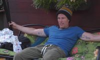 Christian Lell sitzt mit Mütze und blauem T-Shirt im Garten von Promi Big Brother.