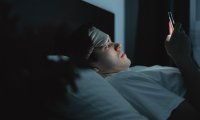 Symbolbild: Ein Mann liegt nachts im Bett und schaut auf sein Smartphone.