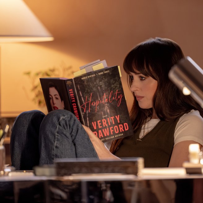 Szenenbild aus „Verity“: Lowen Ashleigh sitzt mit angezogenen Beinen in einem Sessel und liest konzentriert in einem mit zahlreichen Notizzetteln versehenen Buch.