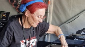 DJ Elly mit roten Haaren und blauen Kopfhörern am Mischpult.
