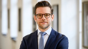 Felix Heinrichs im Anzug vor einem hellen Säulengang