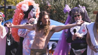 Filmstill aus Hunky Jesus: Jesus-Darsteller mit ausgebreiteten Armen zwischen den Sisters of Perpetual Indulgence