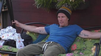 Christian Lell sitzt mit Mütze und blauem T-Shirt im Garten von Promi Big Brother.