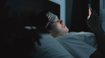 Symbolbild: Ein Mann liegt nachts im Bett und schaut auf sein Smartphone.