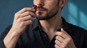 KI-Symbolbild: Ein erwachsener Mann hält ein kleines Poppers-Fläschchen vor blauem Hintergrund an seine Nase.