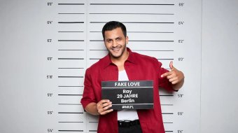 Ray lächelt im roten Hemd beim offiziellen Fotoshooting für „Make Love, Fake Love“.