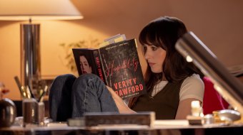 Szenenbild aus „Verity“: Lowen Ashleigh sitzt mit angezogenen Beinen in einem Sessel und liest konzentriert in einem mit zahlreichen Notizzetteln versehenen Buch.