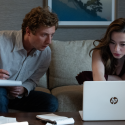Szenenbild aus „The Social Reckoning“: Ein Mann mit Notizblock und eine Frau sitzen auf einem Sofa und betrachten gemeinsam einen geöffneten Laptop.