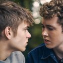 Szenenbild aus dem Film „Free at Heart“: Zwei junge Männer sitzen sich im Freien dicht gegenüber und schauen einander an.