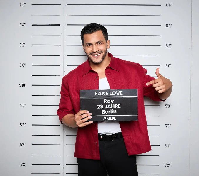 Ray lächelt im roten Hemd beim offiziellen Fotoshooting für „Make Love, Fake Love“.