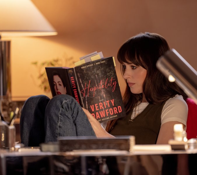 Szenenbild aus „Verity“: Lowen Ashleigh sitzt mit angezogenen Beinen in einem Sessel und liest konzentriert in einem mit zahlreichen Notizzetteln versehenen Buch.